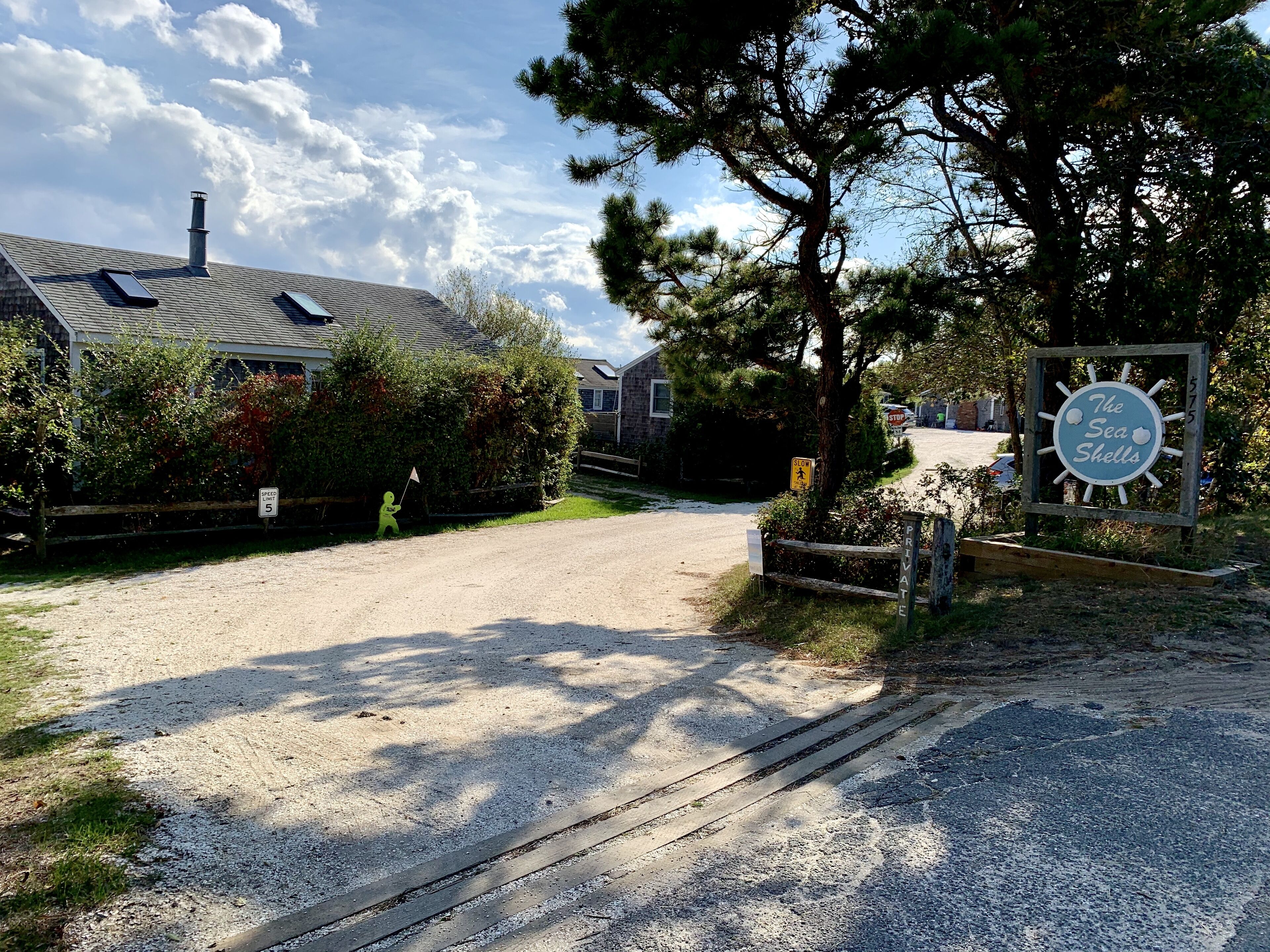 A gravel driveway leading to a house with a 'PRIVATE' sign, a 'SLOW' speed limit sign, and a sign for 'The Sea Shells'.