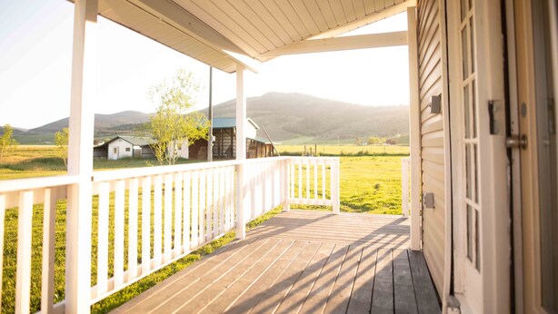 Een houten veranda met een witte balustrade, leidend naar een huis met uitzicht op de bergen.
