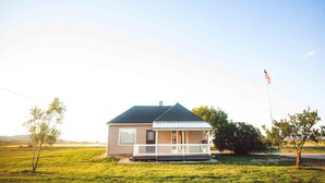Een gelijkvloers huis met een veranda, een vlaggenmast met een Amerikaanse vlag en een grasveld op de achtergrond.