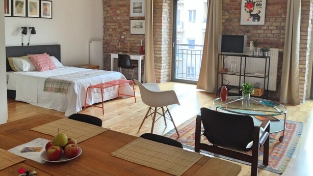 A modern bedroom with a large bed, a desk, and a dining area with a table set for two. - Stylish loft near the Danube (Budapest)