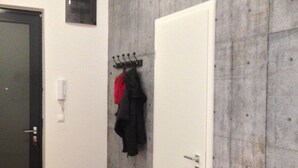 A room with a wooden chest, a coat rack with jackets, a white door, and a textured wall. - Stylish loft near the Danube (Budapest)