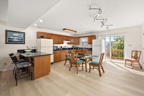 Uma cozinha moderna com armários de madeira, uma área de jantar com cadeiras de vime e vista para o exterior.