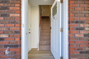 A hallway with a carpeted staircase, white doors, and brick walls.