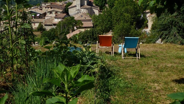 Un villaggio con edifici in pietra tradizionali, una chiesa con un campanile e una zona erbosa con due sedie.