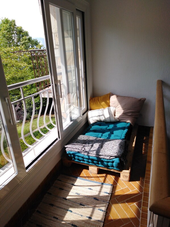 Un petit balcon avec un lit, une fenêtre et une vue sur la verdure.