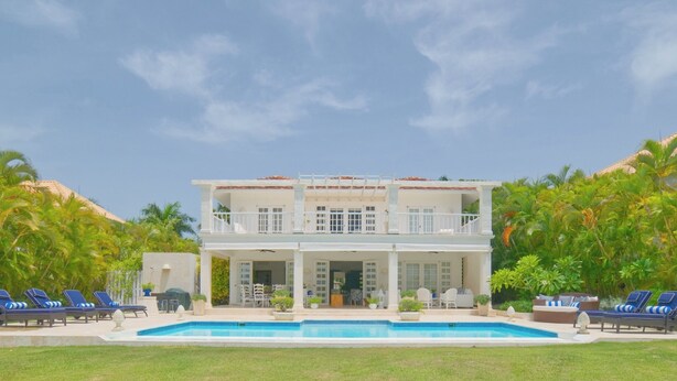 Ein zweistöckiges Haus mit Swimmingpool, umgeben von Palmen und einem klaren Himmel.