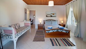 Ein Schlafzimmer mit Holzboden, einem Bett mit Kopfteil, einer Couch, einem Gemälde von Steinen und einem Fenster mit Vorhängen.