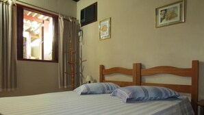 A double bed with striped bedding, a wooden headboard, a bedside lamp, and a window with curtains. - Pousada Seachegue (Ubatuba)