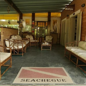 A reception area with wicker furniture, a tiled floor, and a sign that reads 'RECEPCAO'. - Pousada Seachegue (Ubatuba)