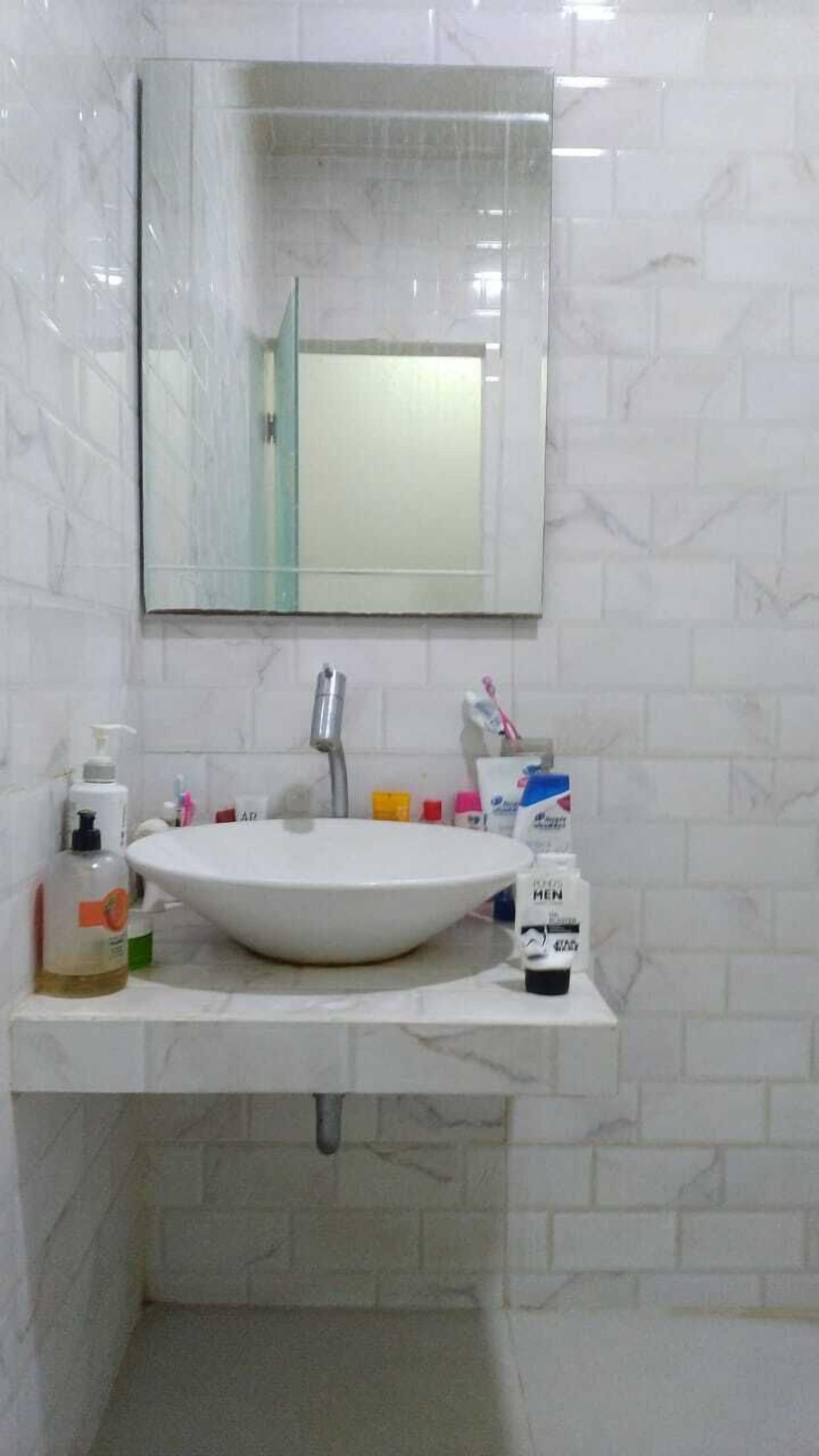 Een badkamer met een wit wastafel, een spiegel en toiletartikelen op het aanrecht.