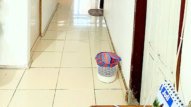 A hallway with a tiled floor, a door labeled '1', a trash bin, and a wall-mounted telephone. - Rachella Homestay (Tanah Datar)