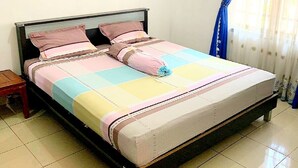 A bed with a colorful quilt, a nightstand, and a window with blue curtains. - Rachella Homestay (Tanah Datar)