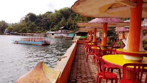 A riverside restaurant with outdoor seating and a boat in the background. - Rachella Homestay (Tanah Datar)