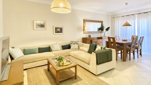 A modern living room with a sofa, coffee table, and dining area. - Amazing apartment in Victoria Boulevard (Vilamoura)