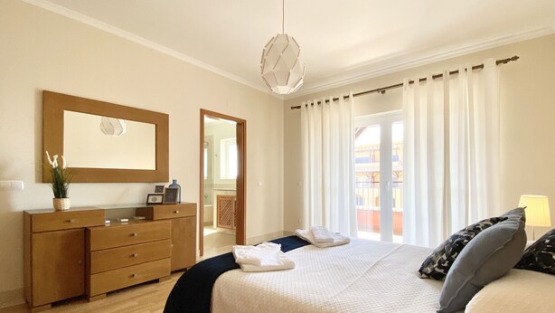 A bedroom with a bed, a dresser, a mirror, and a window with curtains. - Amazing apartment in Victoria Boulevard (Vilamoura)