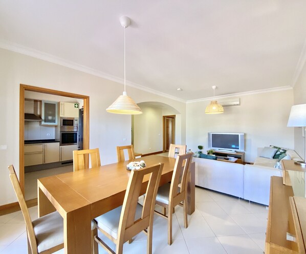 A modern kitchen with white cabinets, a microwave, and a stove. There is a dining area with a wooden table and chairs. - Amazing apartment in Victoria Boulevard (Vilamoura)