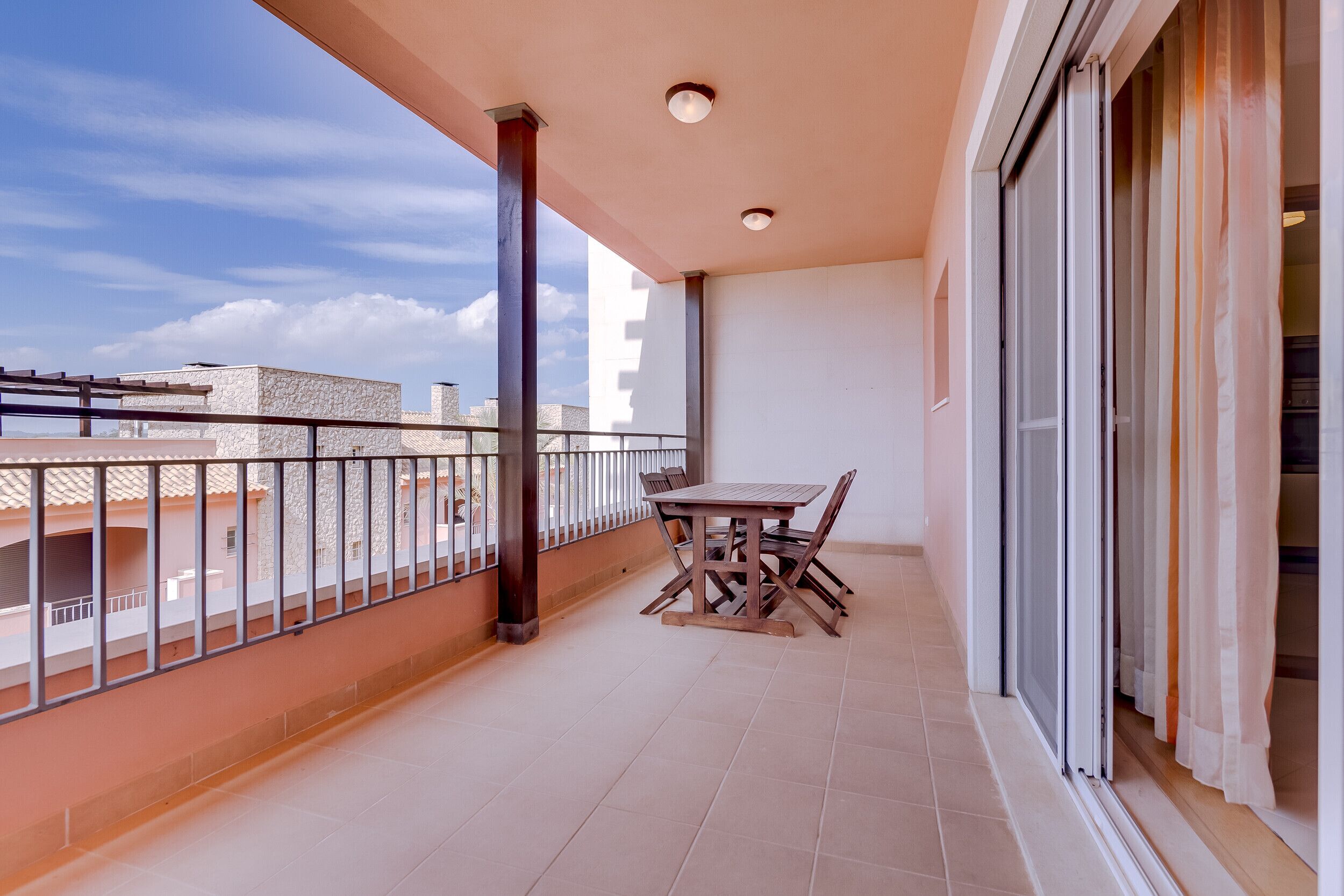 A balcony with a table and chairs, a view of buildings, and a sliding glass door.