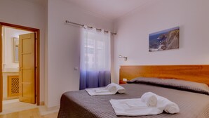 Een hotelkamer met een bed, een houten hoofdbord, een schilderij van een kustlandschap en een badkamer die door een open deur zichtbaar is.