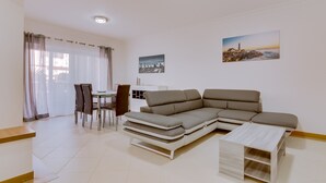 Un salon moderne avec un canapé d’angle, une table à manger avec des chaises et deux tableaux accrochés au mur.