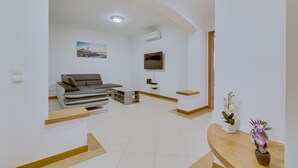 Un salon moderne avec un canapé gris, un téléviseur à écran plat et une petite table ornée de plantes en pot.