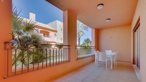 Un balcon donnant sur un immeuble, une table avec des chaises et une rambarde.