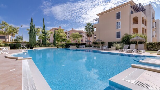 Une piscine avec des chaises longues et un bâtiment doté de balcons.