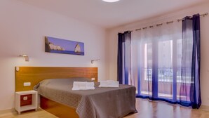 Une chambre à coucher avec un lit, une table de chevet, un tableau et une vue à travers des rideaux légers.