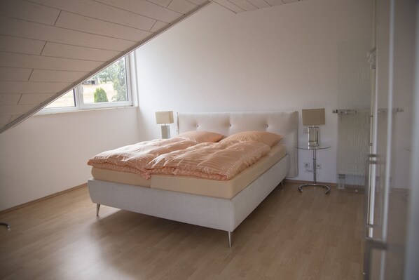 Une chambre à coucher avec un lit, deux lampes de chevet, une petite table et une fenêtre.