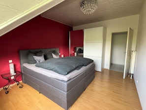 Une chambre à coucher moderne avec un lit gris, des murs rouges et un plancher en bois.