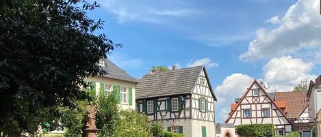 A cobblestone street with traditional half-timbered houses, a statue, and a clear blue sky.