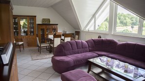 Ein Wohnzimmer mit einem violetten Modularesofa, einem Glastisch und einem Essbereich mit einem Holzkabinett und Stühlen.