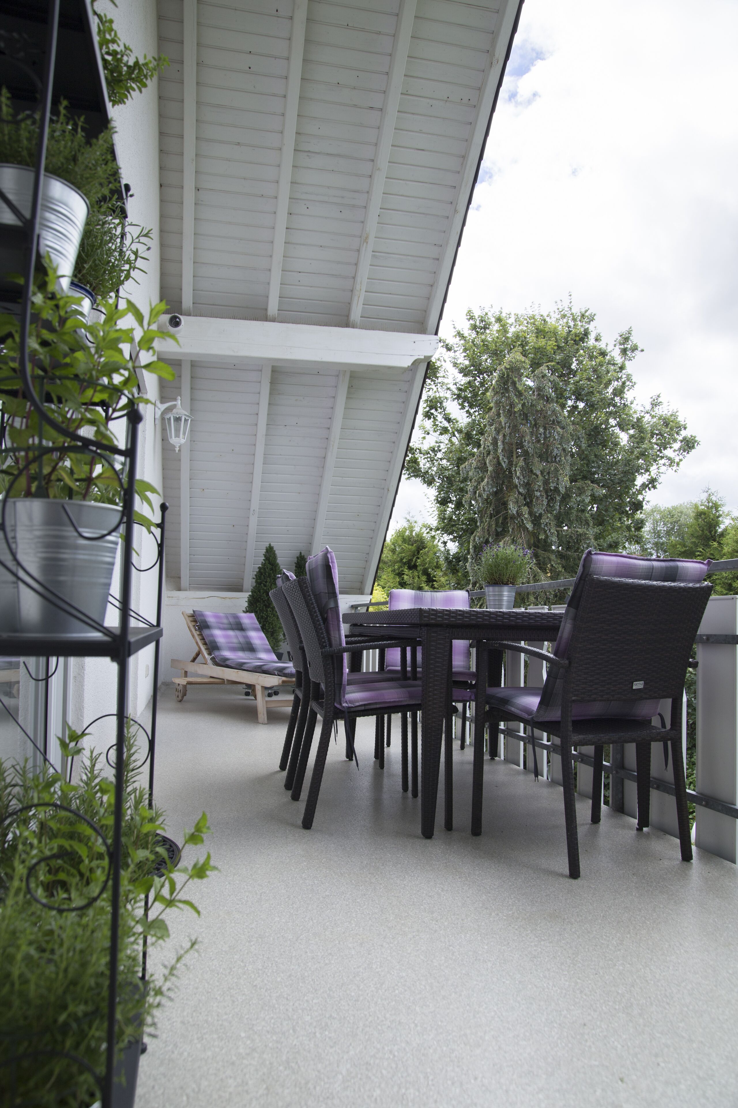 Un patio couvert avec une table et des chaises, entouré de plantes en pot.