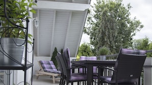 Ein überdachter Patio-Bereich mit Tisch und Stühlen, umgeben von Blumentöpfen.