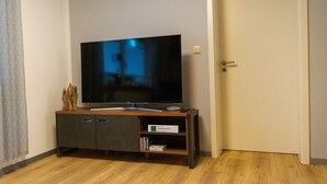 Una stanza con una TV a schermo piatto su un supporto in legno, una porta alla destra e una tenda decorata a sinistra.