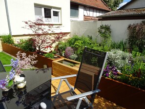 Un jardin avec une terrasse en bois, une chaise et une table agrémentée d’un vase de fleurs.