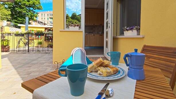 Un patio con una mesa lista para el desayuno, incluyendo un plato de pasteles, una cafetera y una taza.