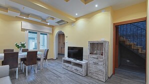 Una sala de estar moderna con comedor, piso de madera y un televisor sobre un soporte de madera rústica.