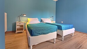 Una habitación con dos camas, piso de madera y una mesita de noche con lámpara.