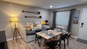 A modern dining area with a wooden table set for four, a sofa with cushions, a lamp, and two decorative paddles on the wall. - Ocean Block Gem in North Ocean City (Ocean City)