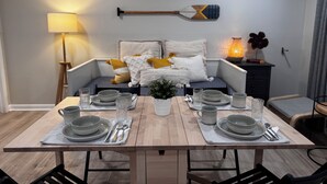 A dining area with a wooden table set for four, a sofa with cushions, a lamp, and two decorative paddles on the wall. - Ocean Block Gem in North Ocean City (Ocean City)