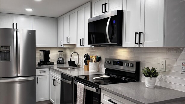 A modern kitchen with stainless steel appliances, white cabinetry, and a grey countertop. - Ocean Block Gem in North Ocean City (Ocean City)