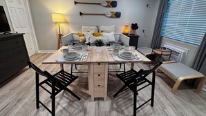 A dining area with a wooden table set for four, black chairs, a small bench, and a TV on a dresser. - Ocean Block Gem in North Ocean City (Ocean City)