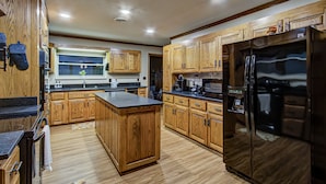 A kitchen with wooden cabinets, a central island, a black refrigerator, and a window above the sink. - Kenny's Mountain Hideaway w/ Hot Tub, Arcade, Fireplace, Views, & 10 King Beds (Sevierville Tennessee)
