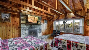 A cabin with two beds, a stone fireplace, wooden walls, and a large window. - Kenny's Mountain Hideaway w/ Hot Tub, Arcade, Fireplace, Views, & 10 King Beds (Sevierville Tennessee)
