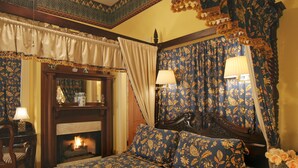 Une chambre à coucher de style traditionnel, avec une cheminée, des rideaux décoratifs et une literie à motifs floraux.