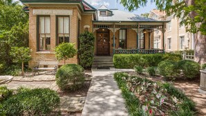 Une maison à deux étages avec un porche à l’avant, une façade en briques et un jardin bien entretenu.