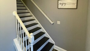 Una escalera con barandillas blancas y peldaños negros que conduce a una plataforma donde se encuentra un cartel que dice 'disfruta de las pequeñas cosas'.