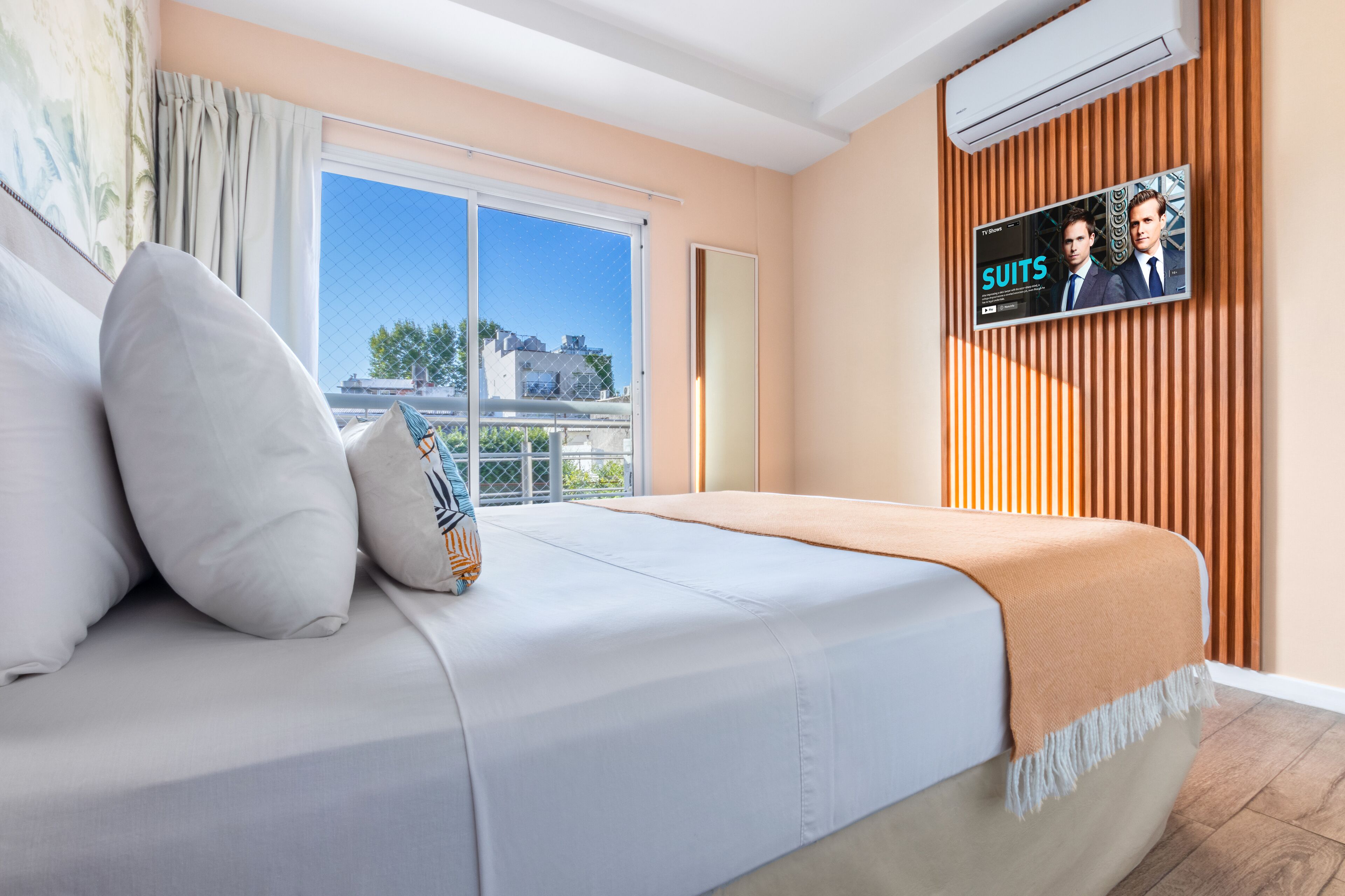 Habitación de hotel con cama, televisor montado en la pared, ventana con vistas y equipo de aire acondicionado.