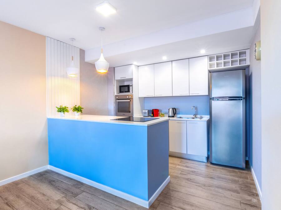 A modern kitchen with a blue island, white cabinets, stainless steel appliances, and a wooden floor.