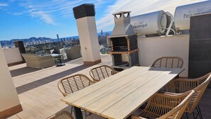 An outdoor patio with a long table and wicker chairs, a barbecue grill, and a solar water heater. - Modern Penthouse with a sea view. (Finestrat)